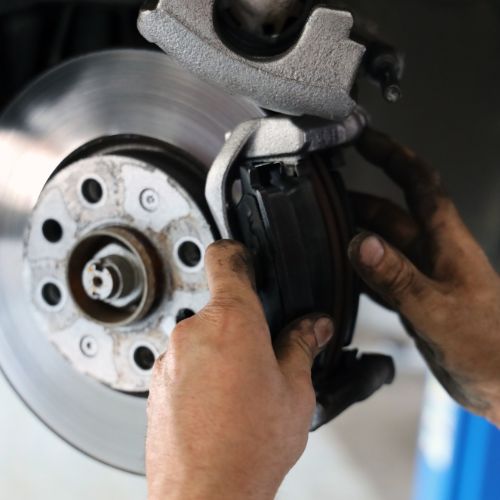 Country Diesel Mechanics | A close-up of a person’s hands installing or removing a brake pad on a car’s brake disc, with visible dirt on the hands—a clear sign of tackling common car issues. | Alice Springs