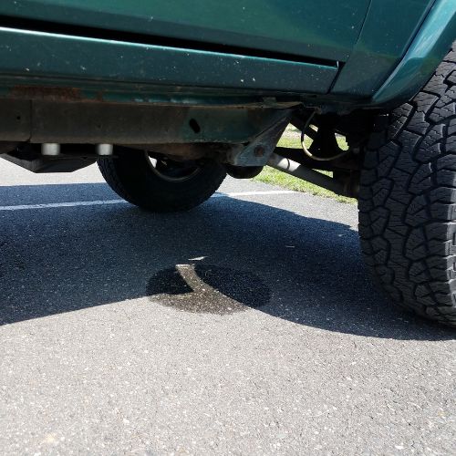 Country Diesel Mechanics | A close-up view of the underside of a green vehicle parked on asphalt in the Northern Territory, showing a fresh dark fluid leak forming a puddle beneath the front section—a sign of common vehicle issues. | Alice Springs